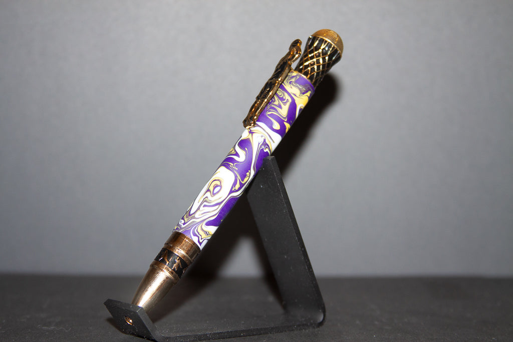 Decorative pen with purple and gold design on a black stand against a gray background