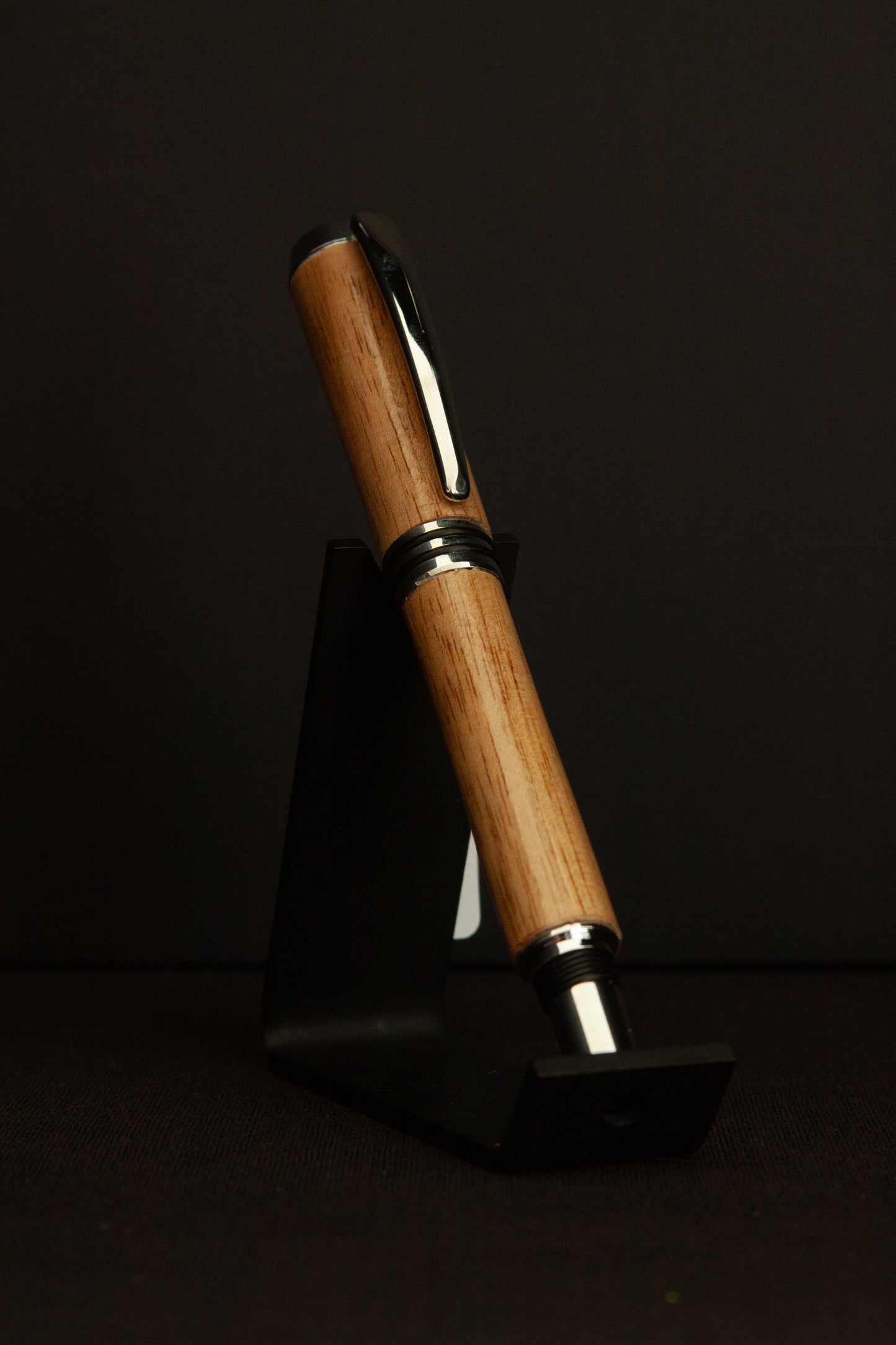 Wooden pen with silver clip on a black stand against a black background